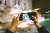 Foto: To hender som holder en mobil og fotograferer Fontana di Trevi i Roma.