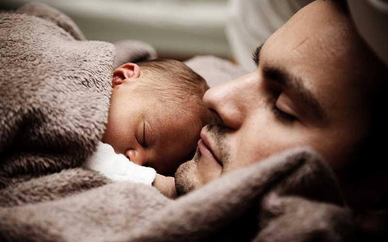 En pappa holder sitt nyfødte barn tett inntil sitt bryst.