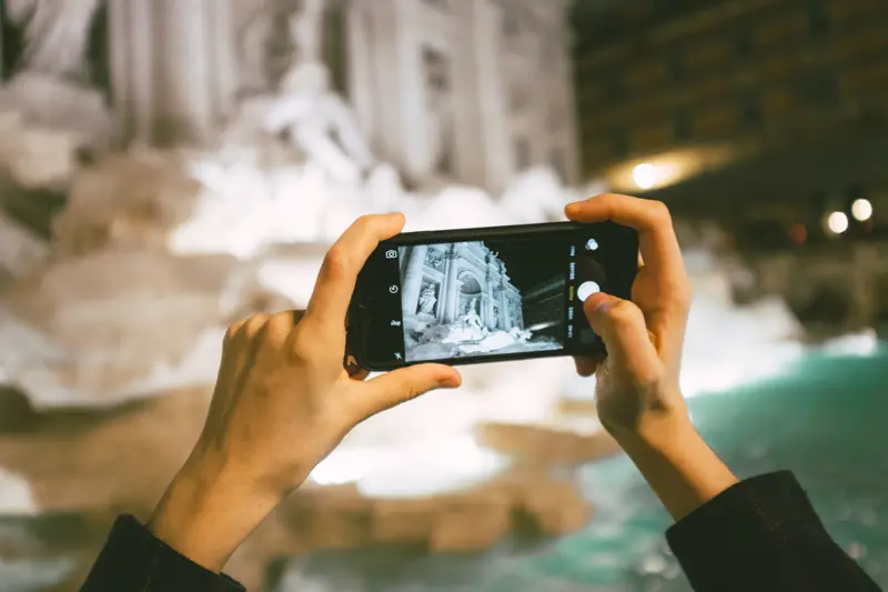 Foto: To hender som holder en mobil og fotograferer Fontana di Trevi i Roma.